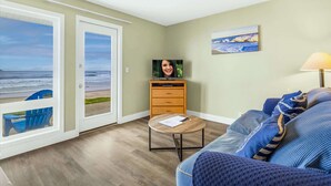 A living room with a view of the beach, a television, a lamp, and a sofa with cushions.