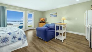 A bedroom with a large window, a bed, a chair, a nightstand, and a lamp.