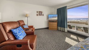 Hotelkamer met een leren bank, een televisie, een klein houten kastje en een balkon met uitzicht op het strand.