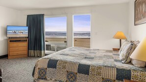 Een hotelkamer met een bed, een televisie, een bureau en uitzicht op het strand.
