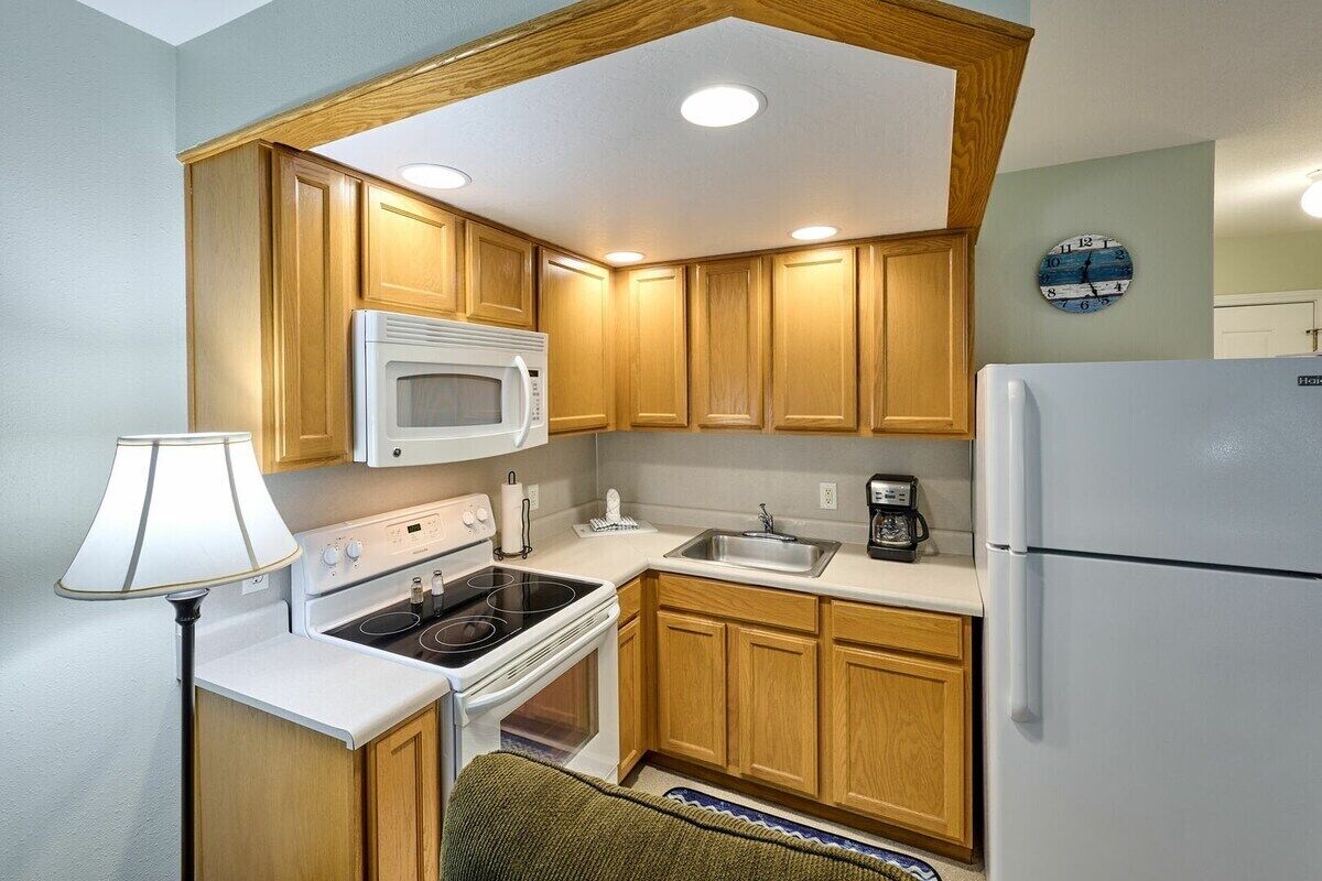 A compact kitchen with wooden cabinets, a microwave, stove, sink, and a refrigerator.