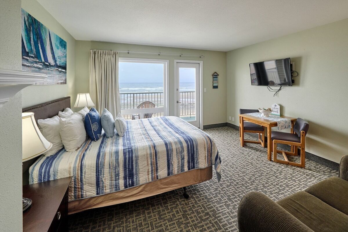 A hotel room with a bed, a desk, a TV, and a view of the ocean.