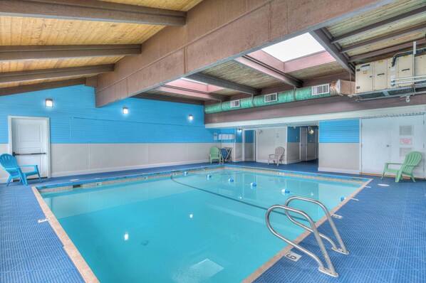 An indoor swimming pool with clear water, blue tiled walls, and a wooden ceiling.