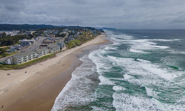A coastal town with a sandy beach, ocean waves, and residential buildings.