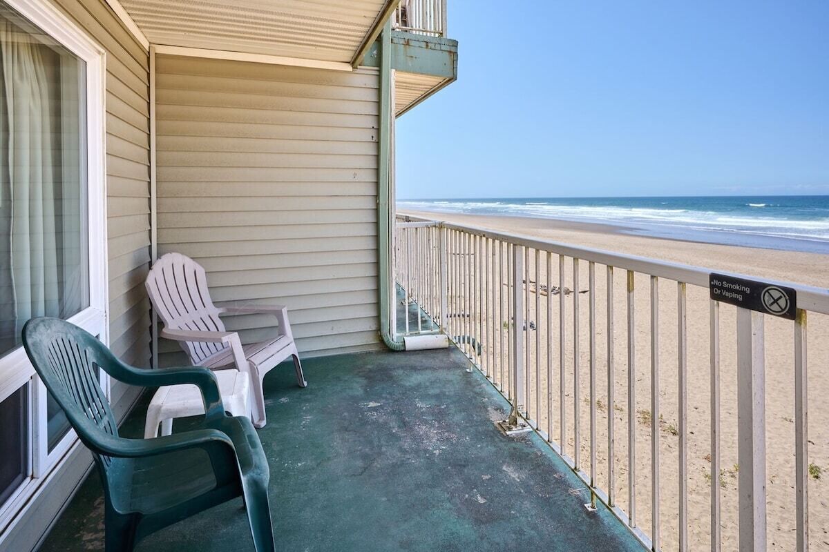 A balcony with a view of the beach, a no-smoking sign, and two chairs.