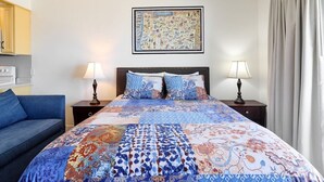 A hotel room with a large bed, two bedside lamps, a headboard, a framed map on the wall, and a blue sofa. - Ground Floor Condo - Ocean View - Pool & Hot Tub! (Lincoln City)