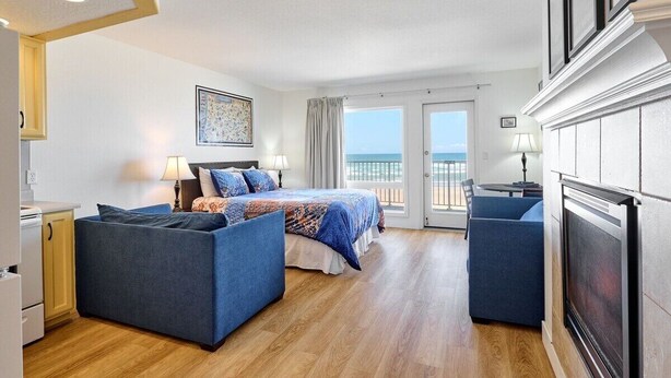 A hotel room with a bed, a sofa, a fireplace, and a view of the ocean. - Ground Floor Condo - Ocean View - Pool & Hot Tub! (Lincoln City)