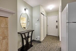 A hallway with a marble column, a round mirror, a dark wooden console table, a patterned carpet, and a white refrigerator. - Fireplace Queen Studio - Ocean View - Pool & Hot Tub! (Lincoln City)