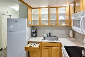A compact kitchen with wooden cabinets, a built-in microwave, a refrigerator, and a coffee maker. - Fireplace Queen Studio - Ocean View - Pool & Hot Tub! (Lincoln City)