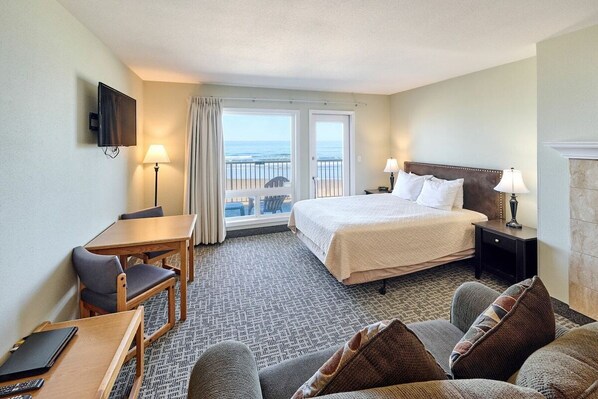 Habitación de hotel con cama, escritorio, silla, televisión y vistas al océano a través de las ventanas.