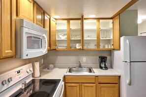 A compact kitchen with wooden cabinets, a microwave, a stove, a sink, and a refrigerator.