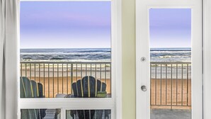A room with a view of the beach and ocean through a window with a metal railing. - Ground Floor Studio - Ocean View - Pool & Hot Tub! (Lincoln City)