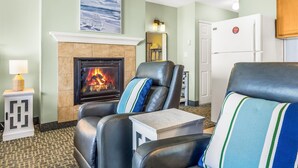 A living room with a fireplace, two leather chairs, a small table, and a lamp. - Ground Floor Studio - Ocean View - Pool & Hot Tub! (Lincoln City)