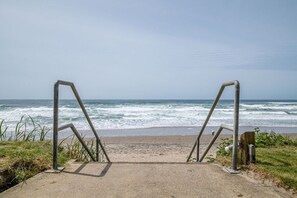 A concrete pathway leading to a beach with metal railings. - Corner Oceanview King Suite, Full Kitchen, Beach Access, Pool & Hot Tub! (Lincoln City)