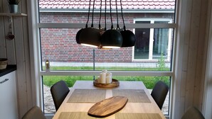 A dining area with a wooden table, black chairs, a hanging light fixture, and a view of a brick building through large windows. - Danish coziness on the Wadden Sea - family and dog friendly. (Jade)