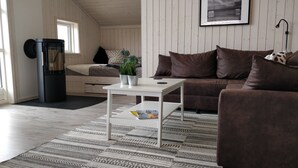 A modern living room with a sofa, a coffee table, and a small table with a magazine. There is a black appliance on the left and a window with blinds. - Danish coziness on the Wadden Sea - family and dog friendly. (Jade)