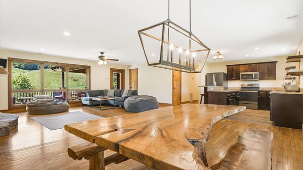 A spacious living area with a large wooden table, a sofa, and a view of a green landscape through large windows.