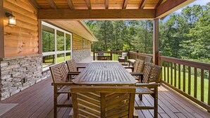 A wooden deck with a table and chairs, stone walls, and a view of a forest.