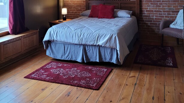 A bedroom with a brick wall, a wooden bed, a ceiling fan, and a window with curtains. - Haven Point is Spacious and Great for Families.  2nd floor apartment. (Strawberry Point)