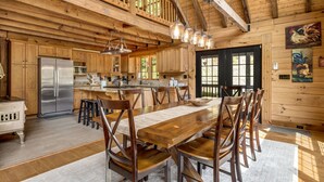 A spacious kitchen with wooden cabinets, a stainless steel refrigerator, and a dining area with a long wooden table and chairs.