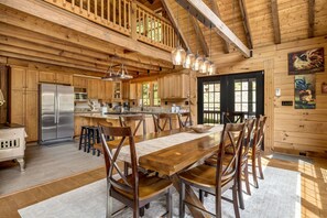 A spacious kitchen with wooden cabinets, a stainless steel refrigerator, and a dining area with a long wooden table and chairs.
