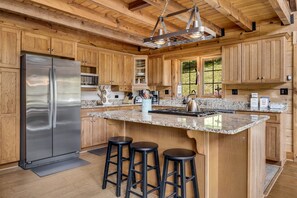 A modern kitchen with wooden cabinets, a stainless steel refrigerator, granite countertops, and a large island with bar stools.