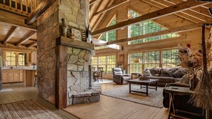 A spacious living area with a stone fireplace, wooden beams, and large windows.