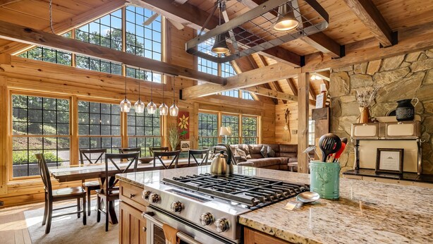 A spacious kitchen with a large island, wooden beams, and a stone wall.
