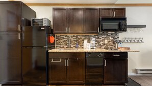 Una cocina moderna con gabinetes de madera oscura, un refrigerador negro, un microondas y un salpicadero de azulejos.