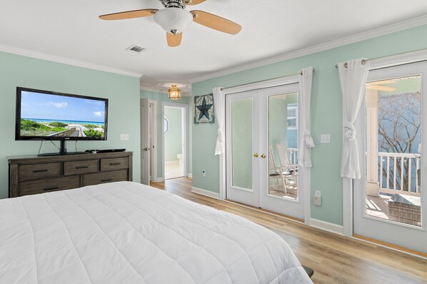 A bedroom with a bed, a television, a ceiling fan, and a view of the outdoors through a sliding door.