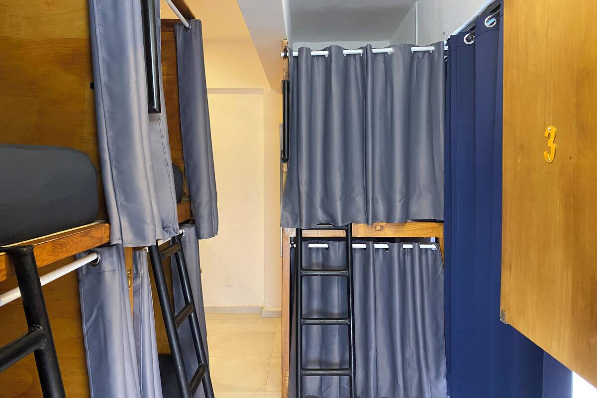 Ein Schlafsaalzimmer mit Etagenbetten, einer Leiter und Vorhängen.