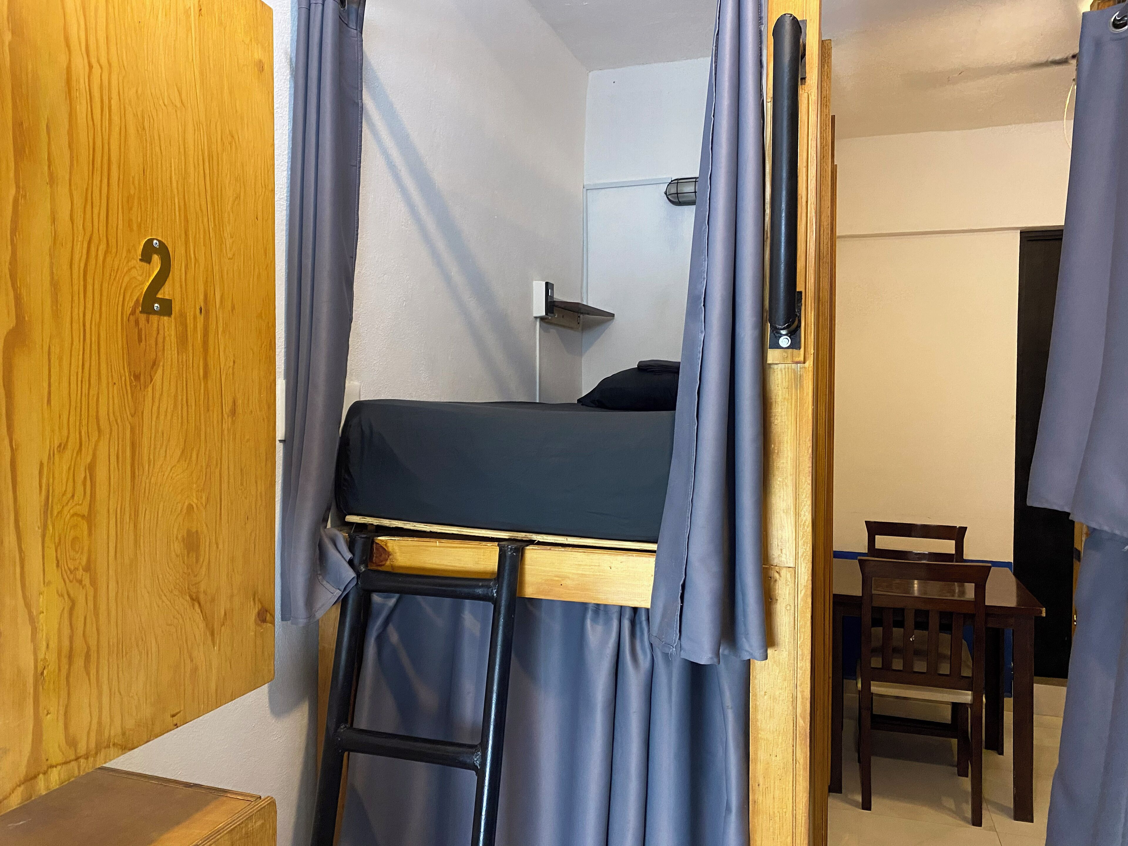 A compact room with a bunk bed, a wooden door with a number, a small table, and a chair.