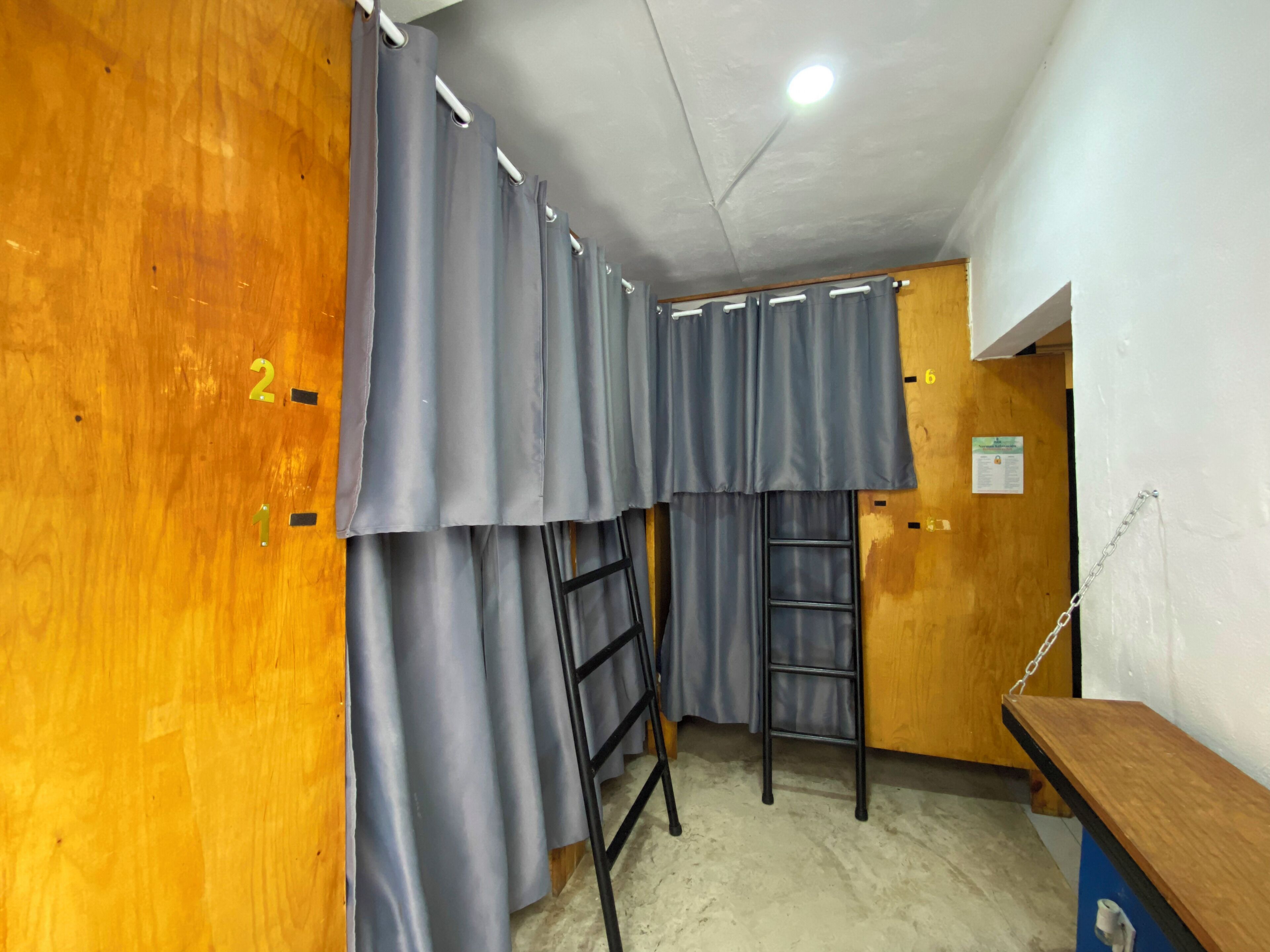 A room with a wooden door, grey curtains, a black ladder, and a wooden bench.