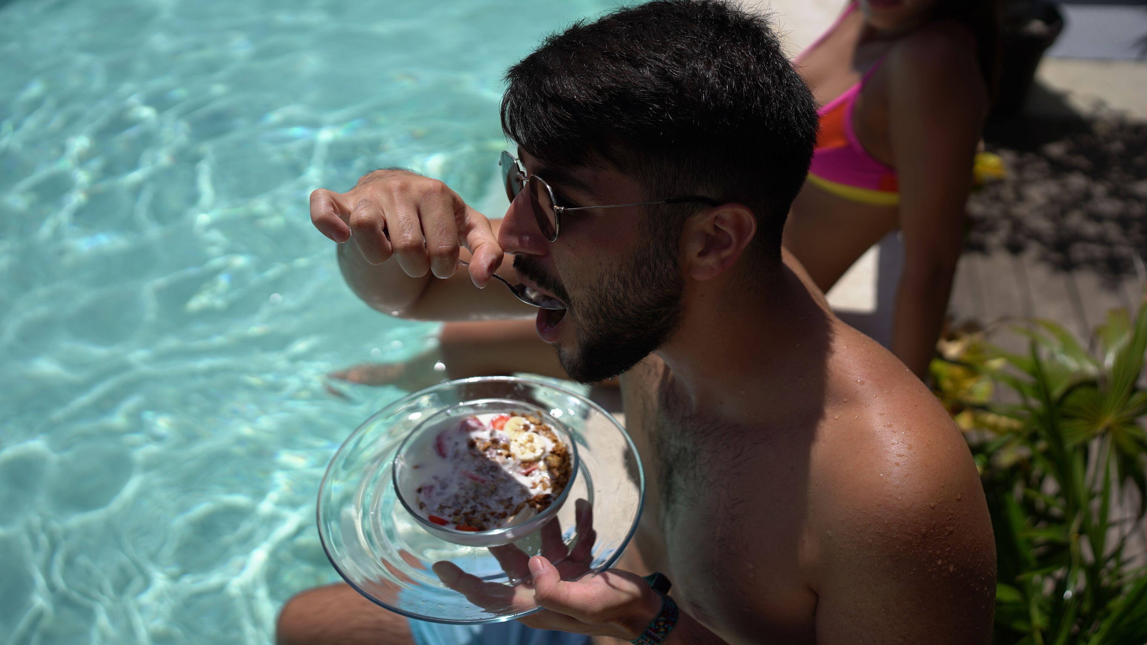 A person holding a glass bowl with a dessert, standing by a pool.