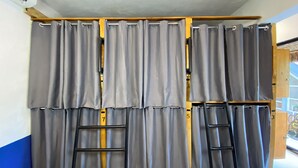 Una habitación con un ventanal grande, cortinas grises y dos escaleras negras apoyadas en la pared.