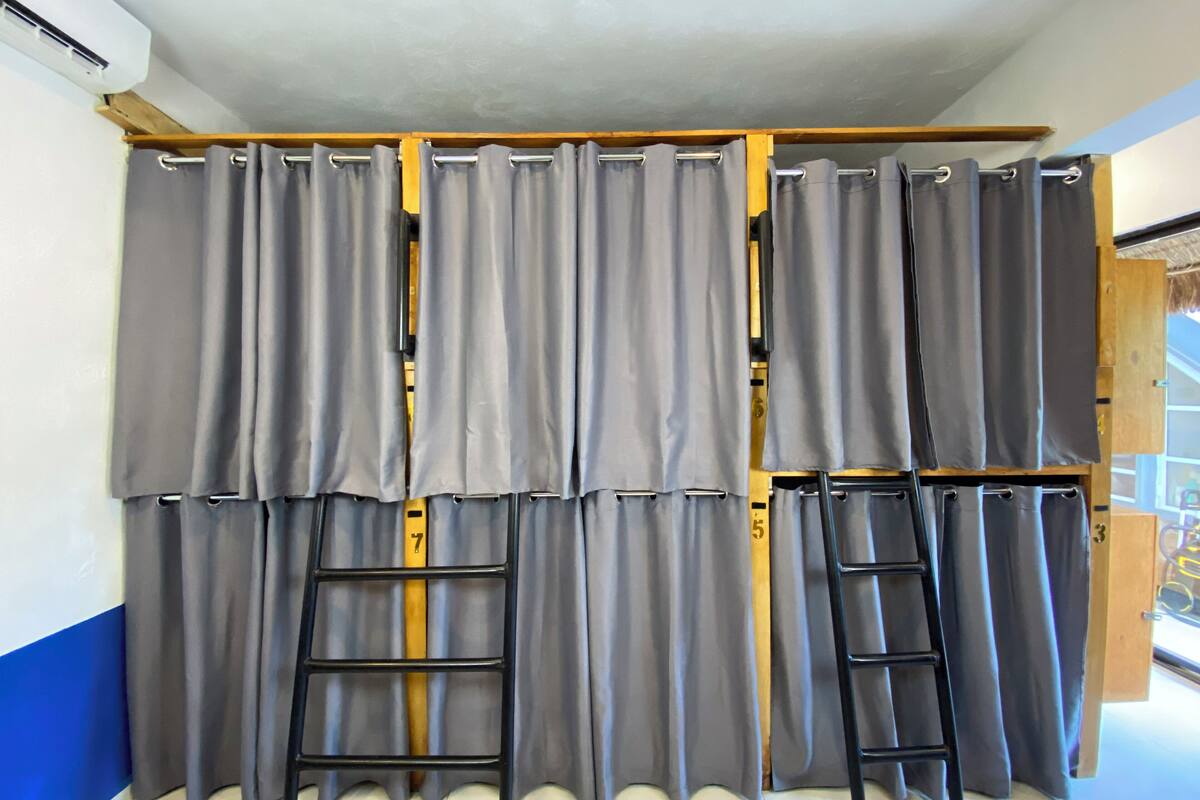 Ein Zimmer mit einem großen Fenster, grauen Vorhängen und zwei schwarzen Leitern, die an der Wand lehnen.
