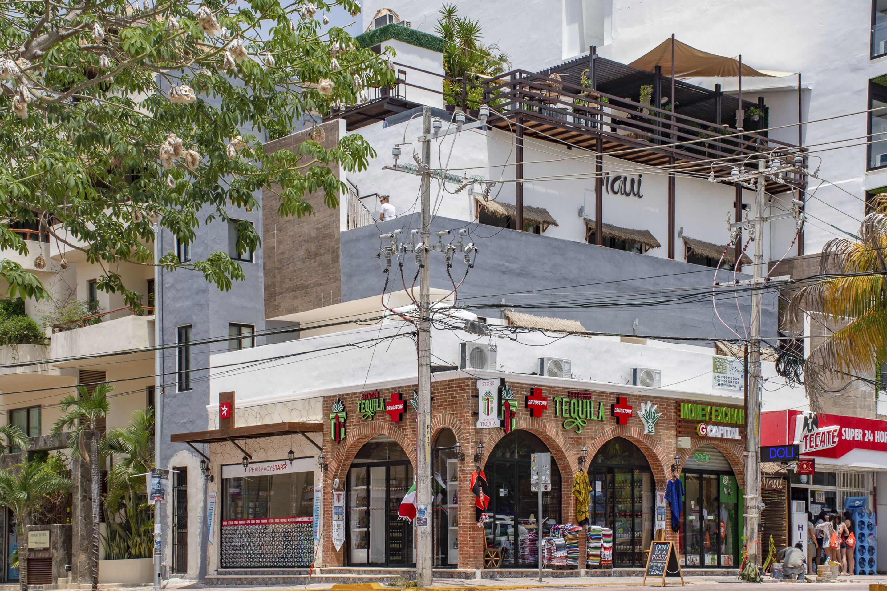 Un immeuble à plusieurs étages, dont le rez-de-chaussée abrite divers commerces, notamment une pharmacie et un magasin reconnaissable à son enseigne en forme de croix rouge.