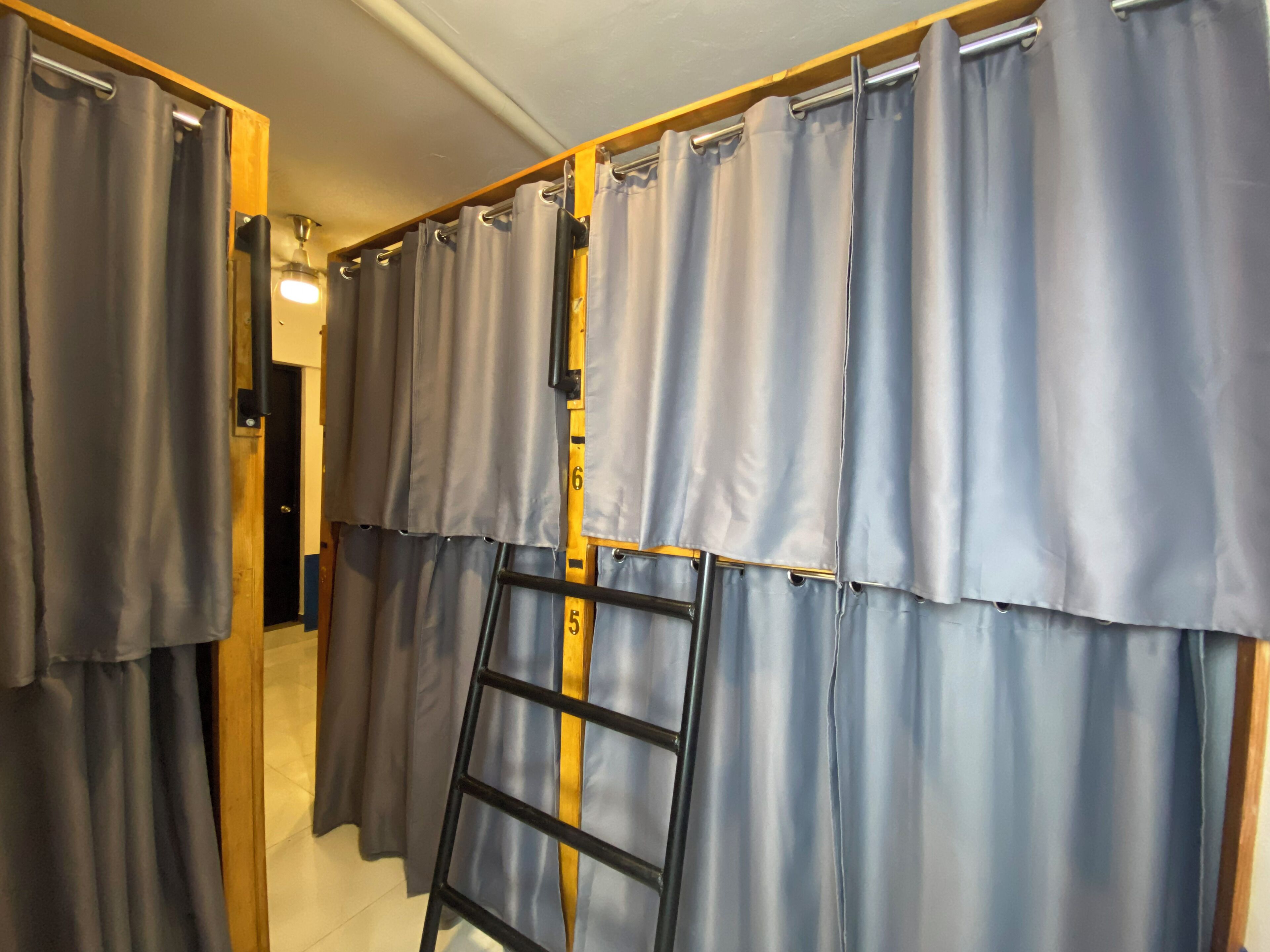 A room with a wooden ladder leaning against a wall of grey curtains.