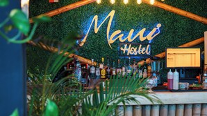 Zona de bar con un letrero de neón que dice 'Manu Hotel', un monitor de computadora y varias botellas.