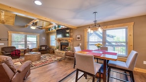 A cozy living room with a fireplace, wooden beams, and a dining area with a table set for four.