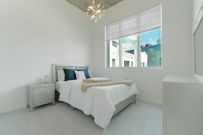 Un dormitorio con cama, mesita de noche, cómoda y ventana con persianas.