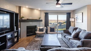 Una sala de estar moderna con chimenea, televisor grande, sofá y vista panorámica de la ciudad.
