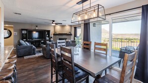 Un salón moderno con televisor grande, asientos cómodos y comedor con vista al exterior.