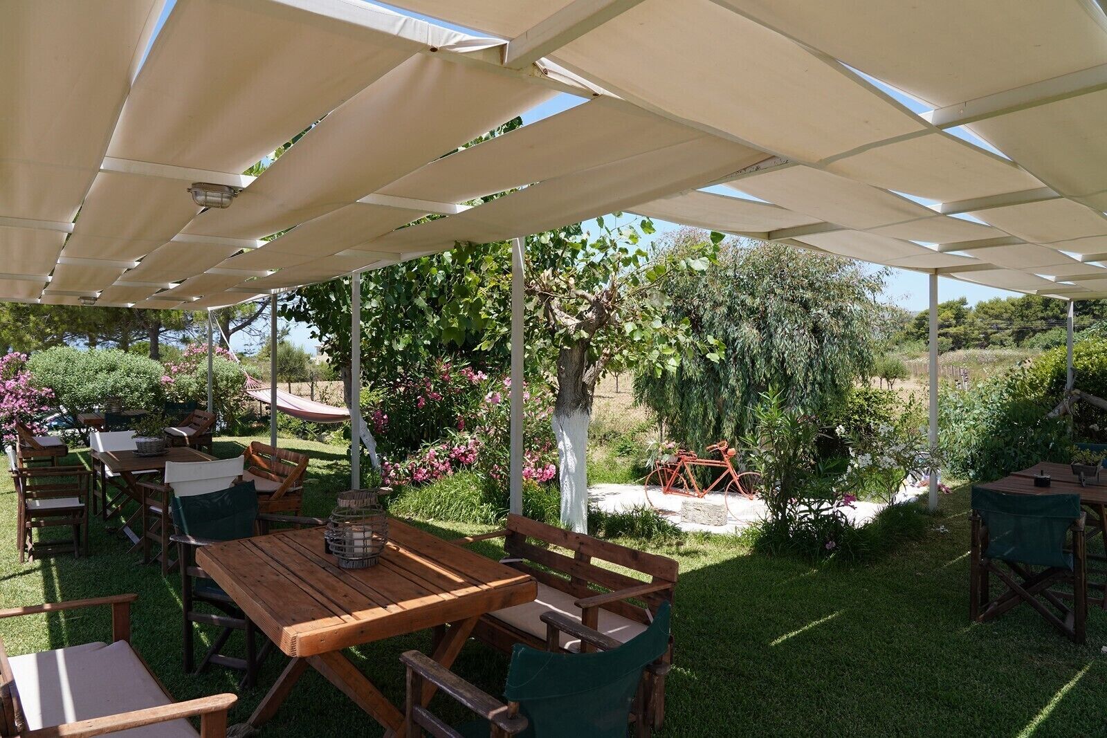 Une terrasse extérieure avec des tables et des chaises en bois, un hamac et un vélo.