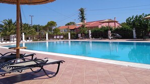Una piscina con suelo de baldosas, sillones de descanso y un toldo de paja.