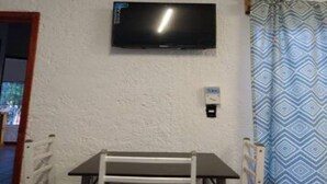 Quarto com televisão presa na parede, mesa com cadeiras e cortina estampada.