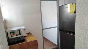 Uma cozinha compacta com micro-ondas, geladeira e uma porta de vidro corria para uma varanda.