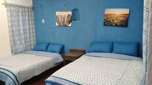 Quarto com duas camas, cada uma com roupa de cama estampada, uma pequena mesa de cabeceira e um ar condicionado fixado na parede.