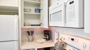 A modern kitchen with white cabinetry, a built-in microwave, a stove, and a coffee maker.