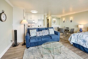 A modern living room with a blue sofa, a glass coffee table, and a kitchen in the background.
